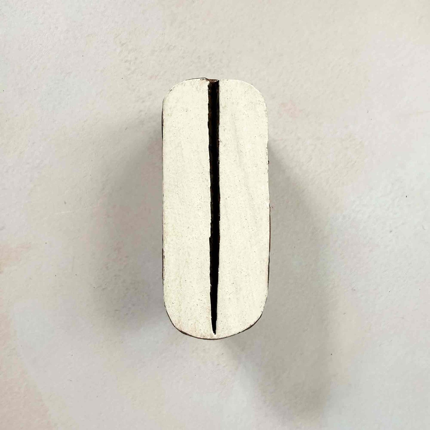 Pod wooden stamp — sleek split-oval design face-on view on soft pale background, single central slit through rounded organic shape, handcrafted Indian printing block