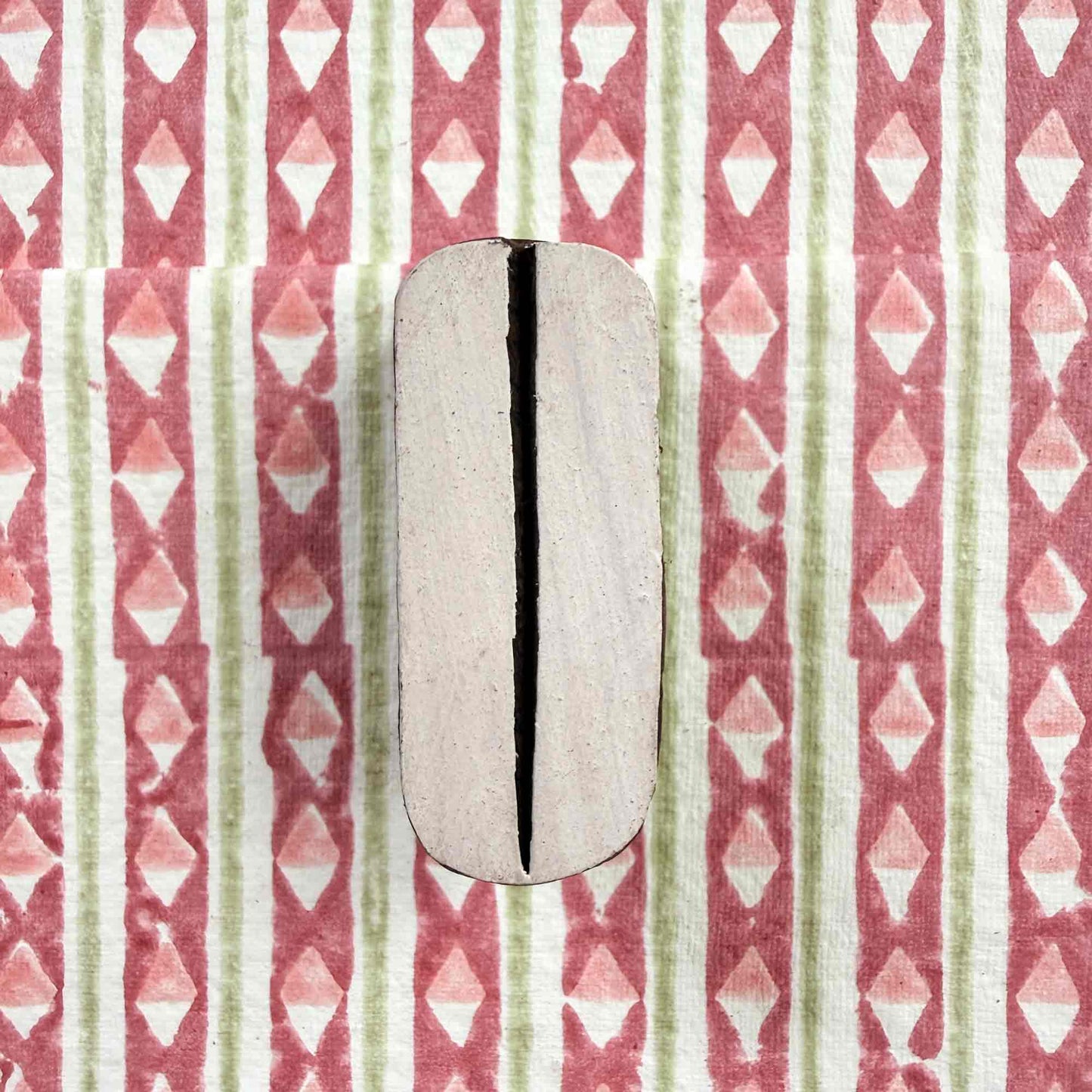 Pod Indian wood block stamp resting on block printed fabric — graceful organic split-oval motif ready for printing, authentic artisan hand-carved block