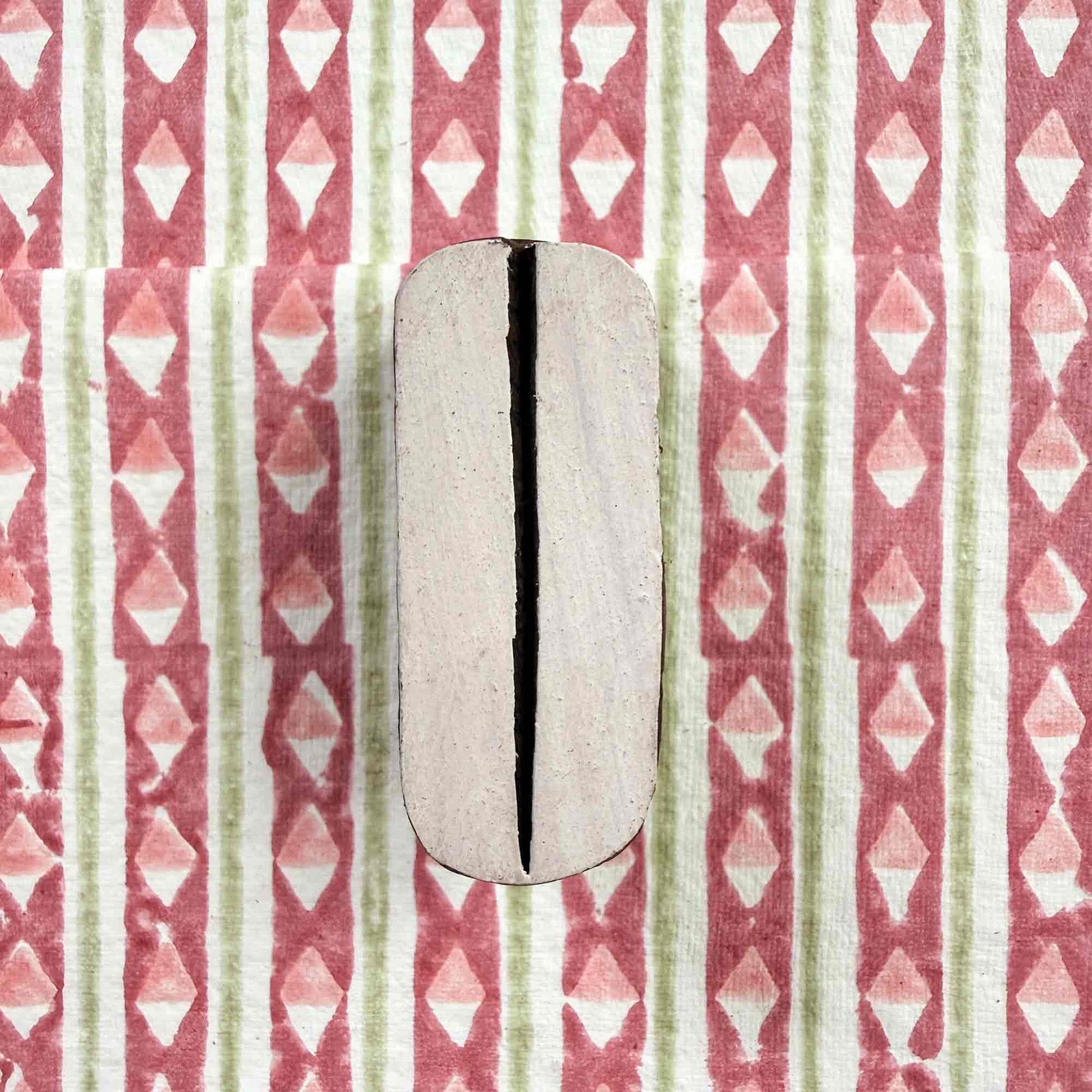 Pod Indian wood block stamp resting on block printed fabric — graceful organic split-oval motif ready for printing, authentic artisan hand-carved block