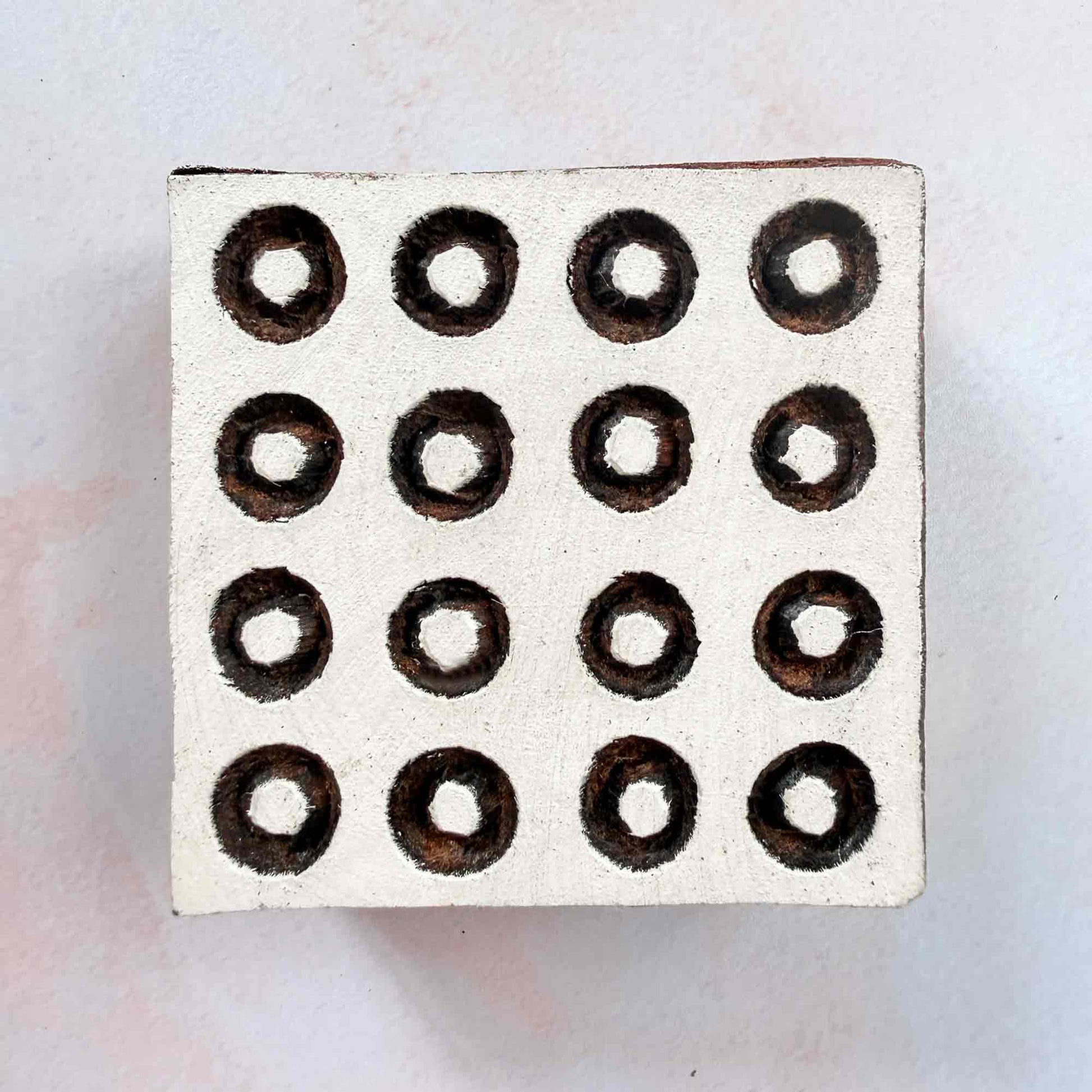 Hand-carved Polkas Indian wood block stamp — square grid of outlined ring dots face-on view on soft pale background, traditional dotted printing block close-up