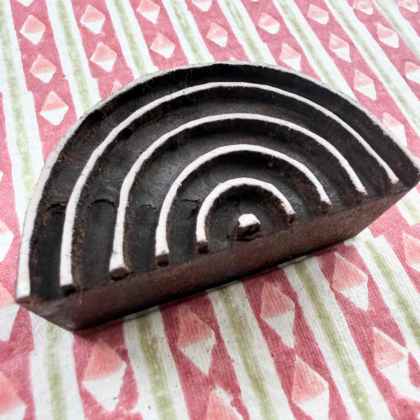Hand-carved Rainbow Indian wood block stamp — semicircular concentric arches resting on block-printed fabric, traditional printing block close-up