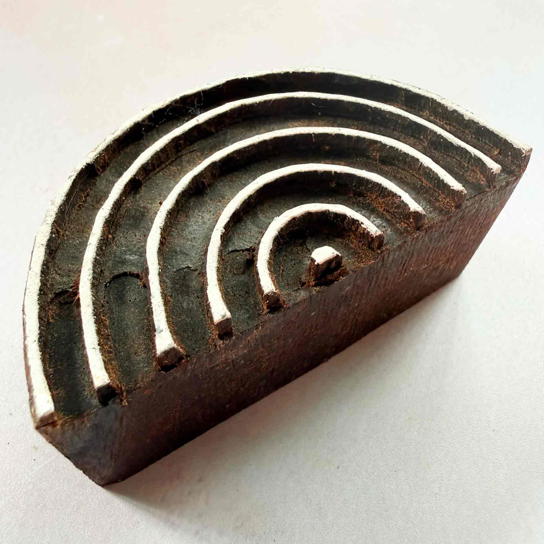 Hand-carved Rainbow Indian wood block stamp — semicircular concentric arches resting on block-printed fabric, traditional printing block close-up
