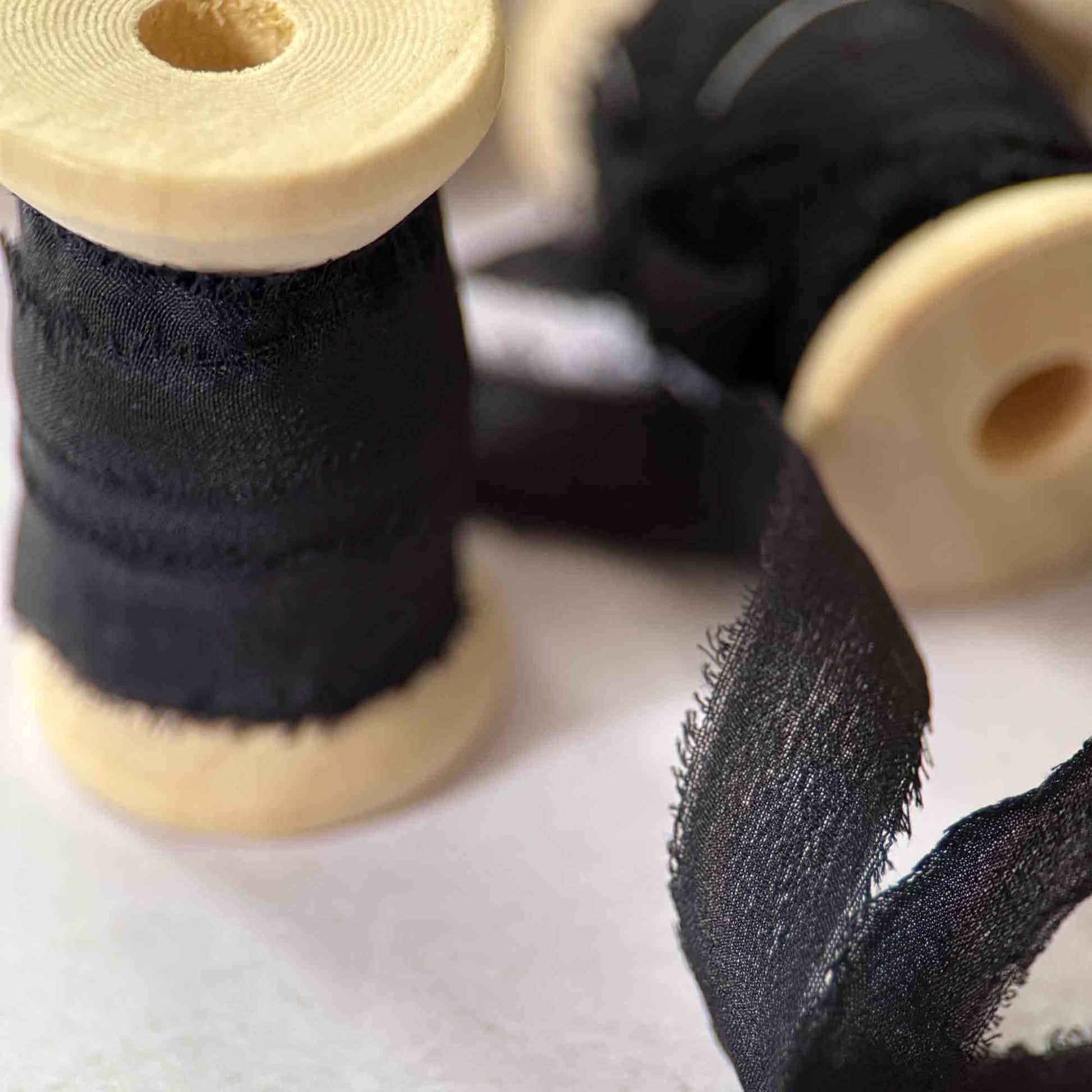 Two spools of black ribbon with wooden cores on a white background