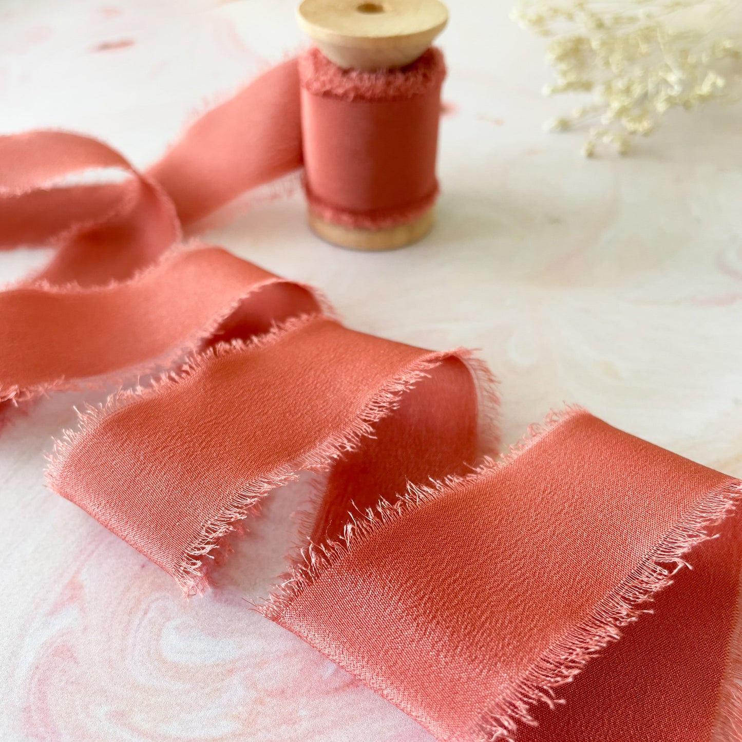 Burnt orange silk ribbon with a frayed edge.  Habotai silk ribbon on a wooden reel.  By The Natural Paper Company.