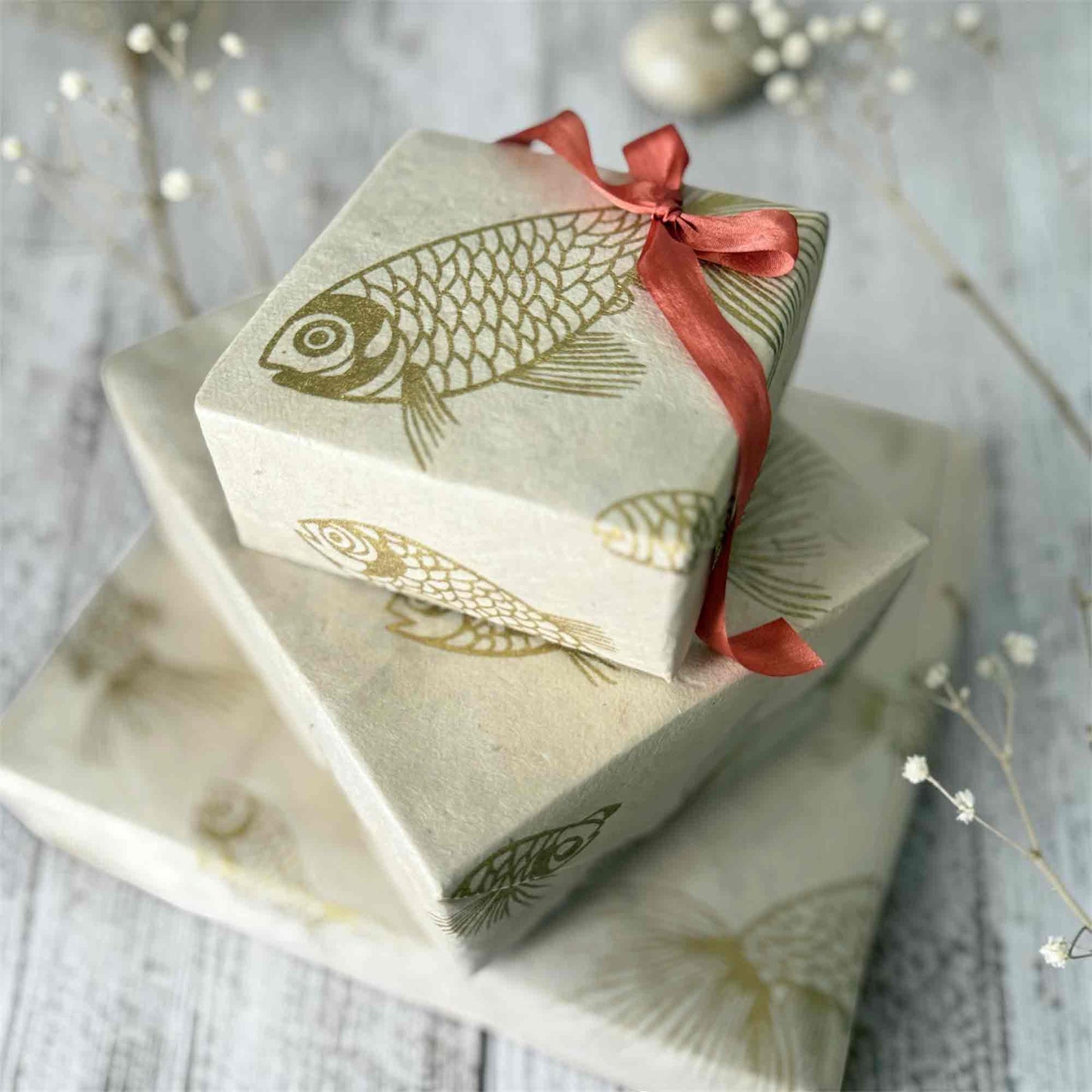 Artisan Lokta paper gift wrap with gold fish design styled on wooden background with dried flowers