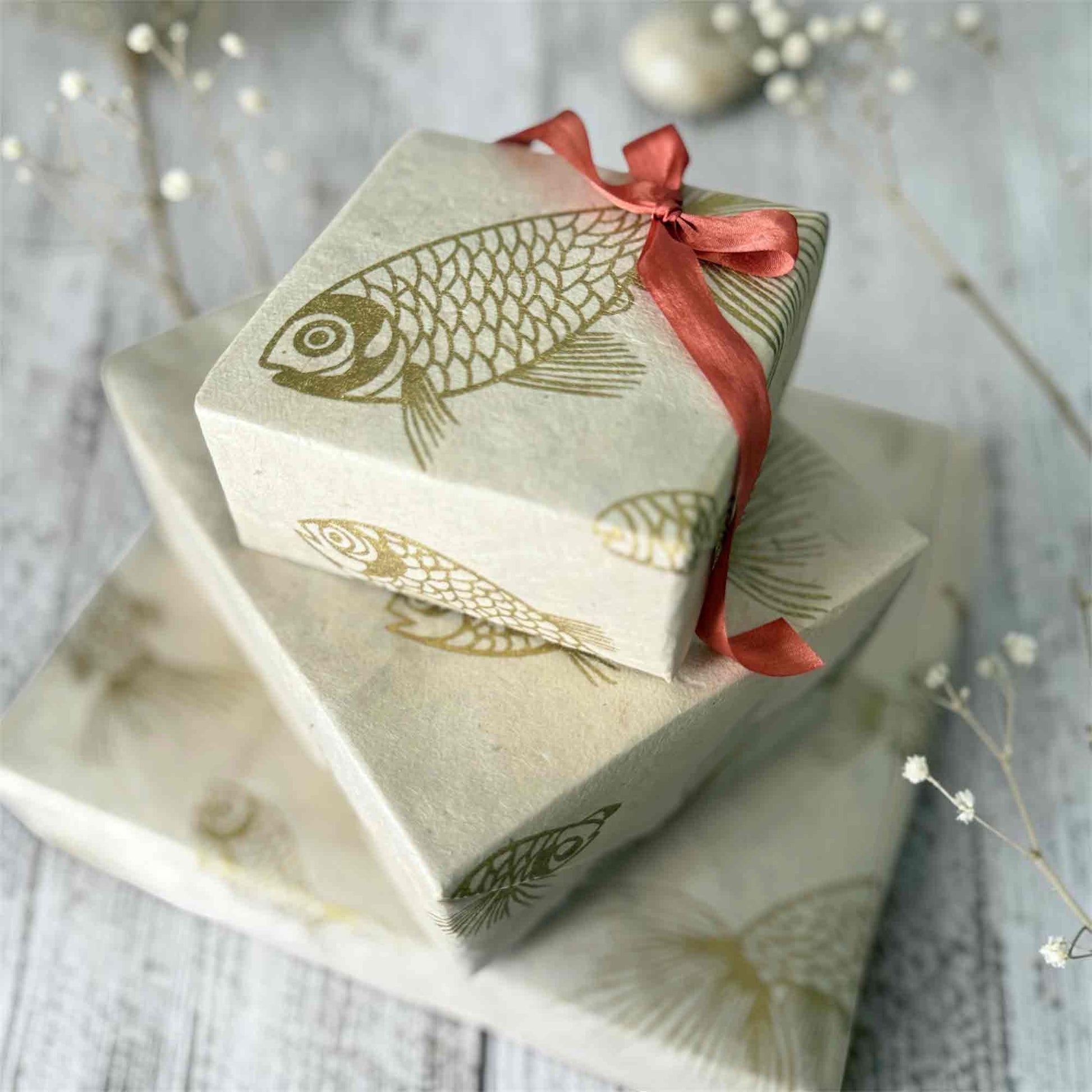 Artisan Lokta paper gift wrap with gold fish design styled on wooden background with dried flowers