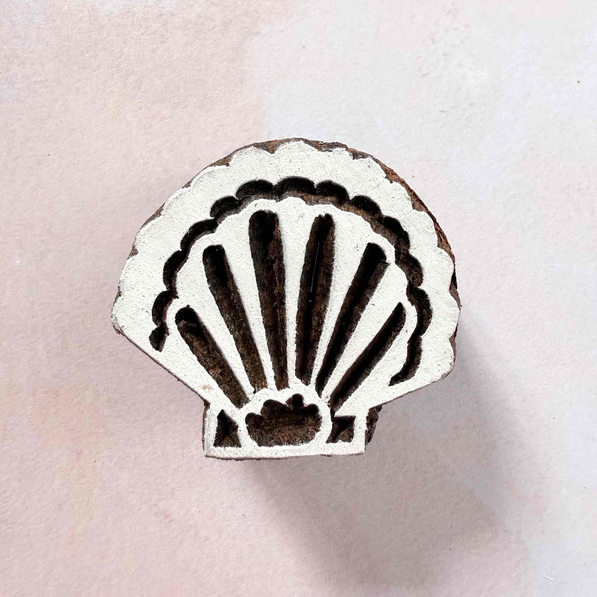 Indian wood block stamp — Shell scallop seashell face-on view on soft pale background, symmetrical curved ribs and delicate rim, hand-carved wooden stamp, classic traditional printing block coastal motif