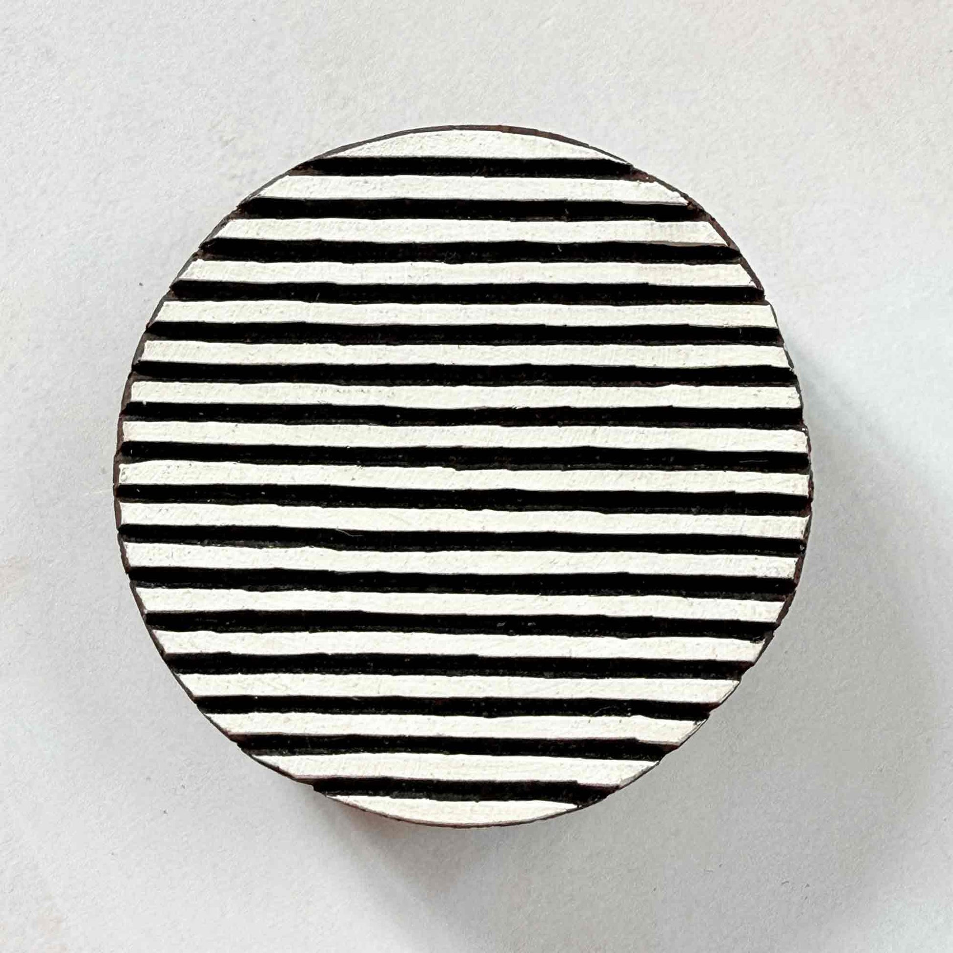 Hand-carved Shield Indian wood block stamp — round shape with fine horizontal stripes face-on view on soft pale background, bold textured motif traditional printing block from India