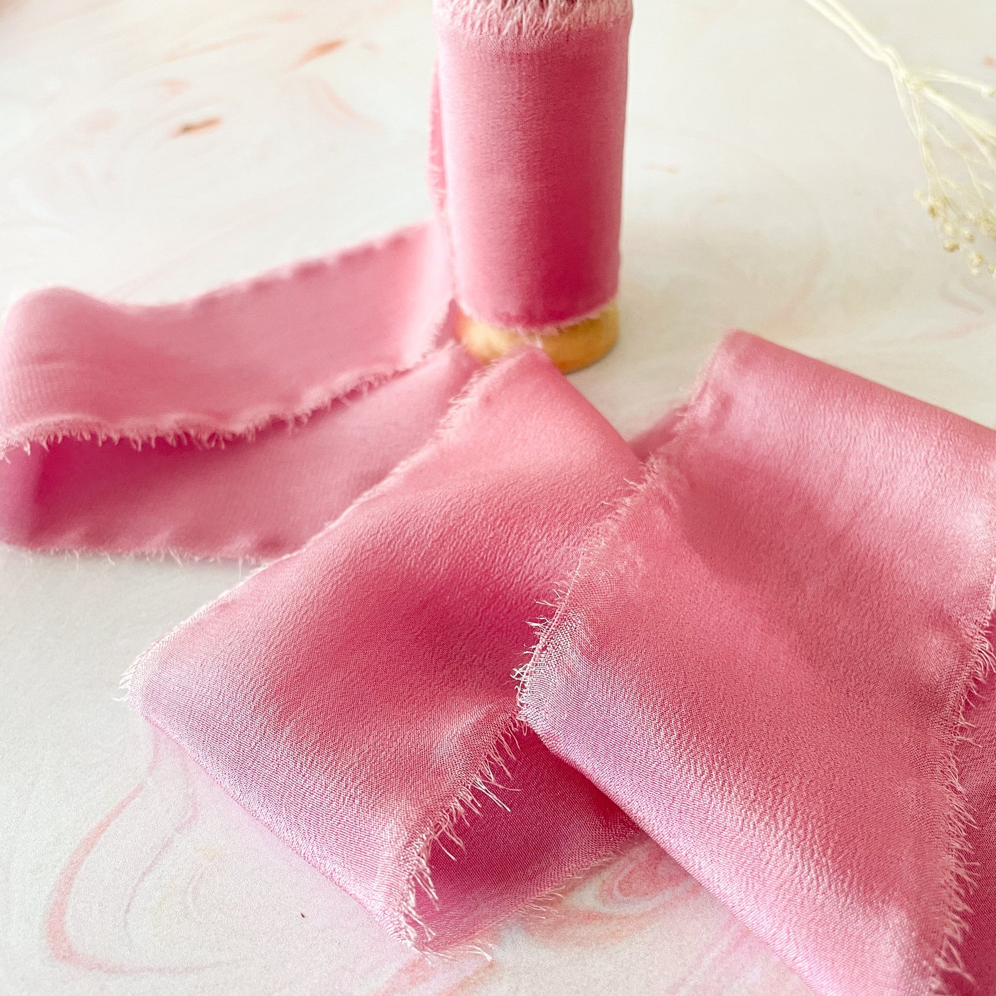 Soft raspberry pink colour silk ribbon with frayed edges.  Luxury silk ribbon By The Natural Paper Company.