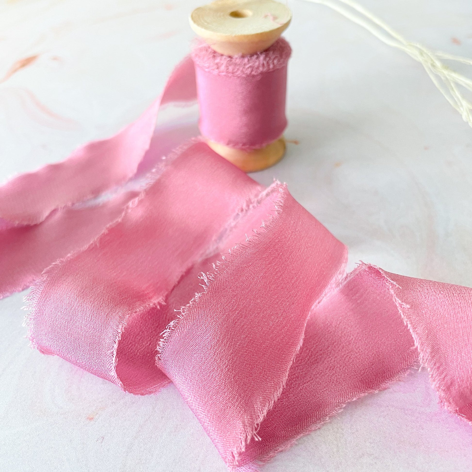 Pink silk ribbon for wedding invitations and stationery.  Raspberry pink colour luxury silk ribbon on a wooden reel.  By The Natural Paper Company.