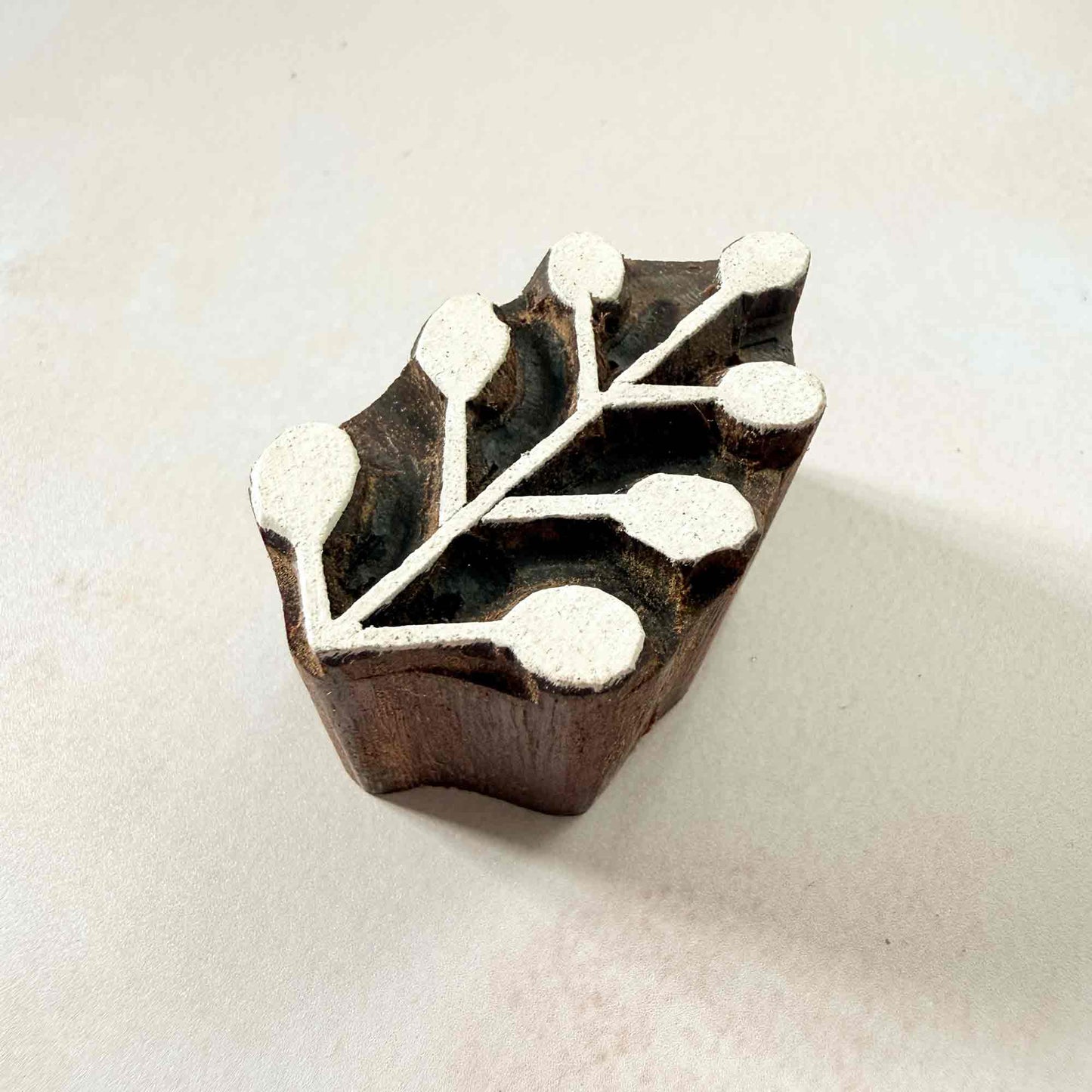 Hand-carved Sprig Indian wood block stamp — delicate berry sprig viewed from side, showing carved depth and smooth rounded berry texture, traditional hardwood printing block from India