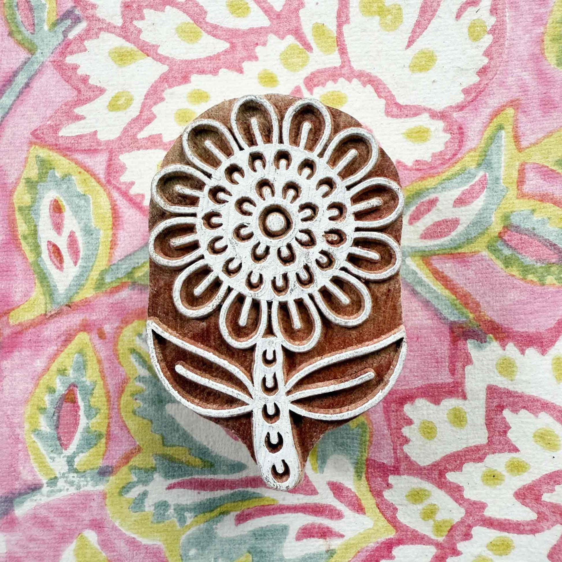 Decorative wooden printing block with floral design on a colorful fabric background