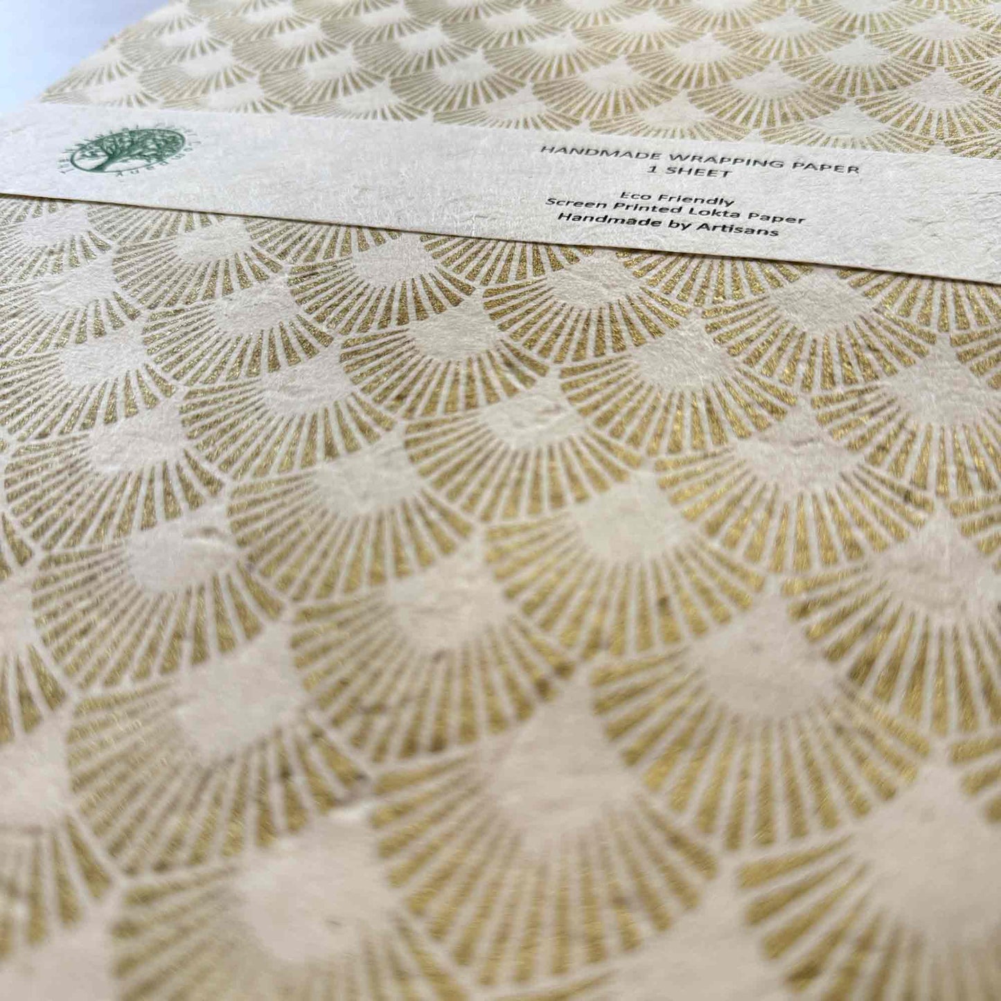 Textured Lokta paper wrapping paper close-up, hand screen printed gold metallic pattern, sustainable artisan gift wrap
