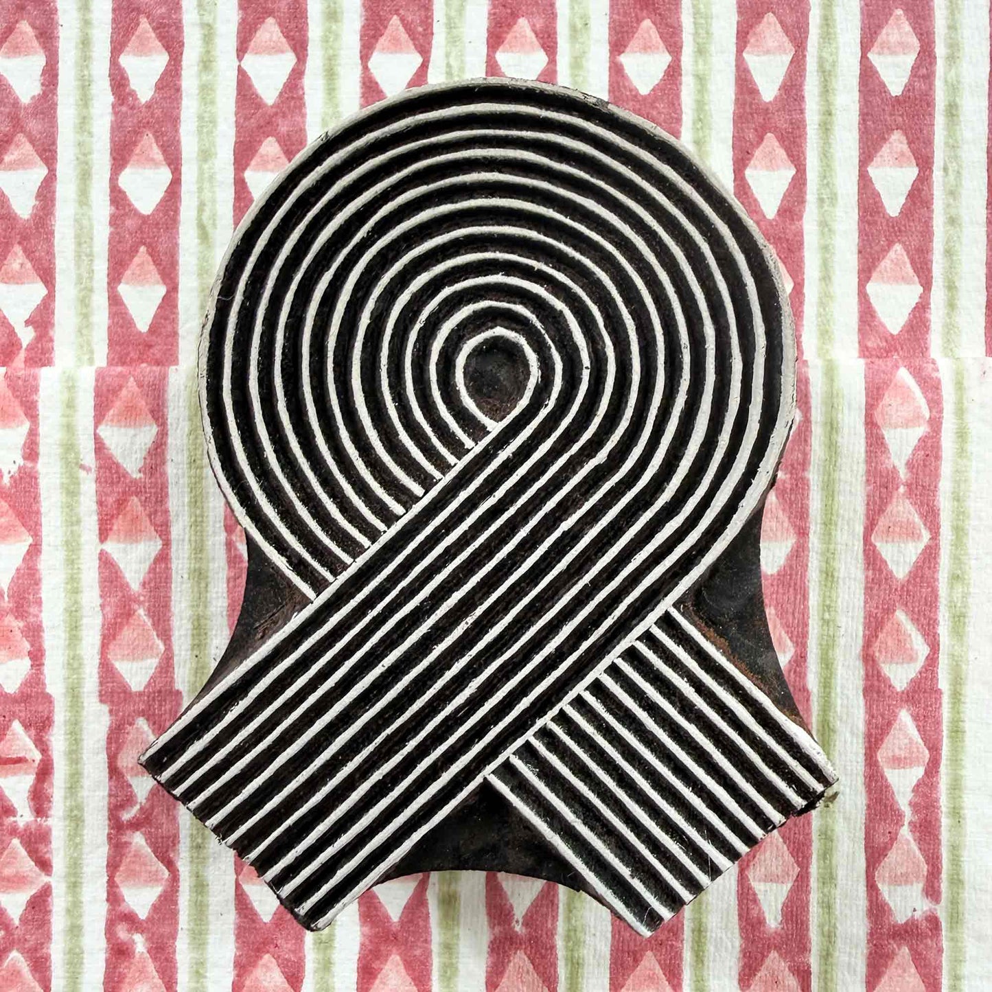 Hand-carved Swirl Indian wood block stamp — spiral ribbon design resting on block-printed fabric, traditional printing block close-up