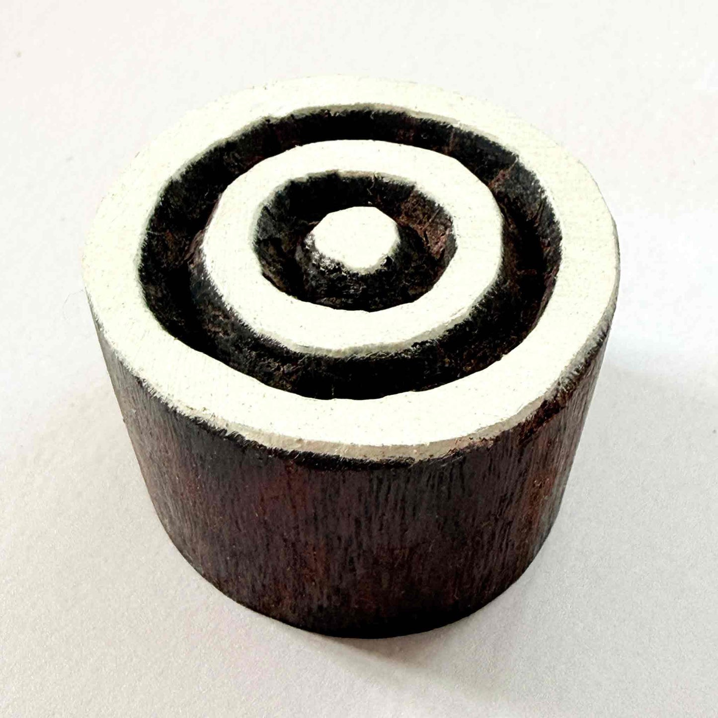 Indian wood block stamp — Target concentric circles resting on red-and-white patterned fabric, central dot and three even rings, hand-carved wooden stamp, classic traditional printing block ready for printing