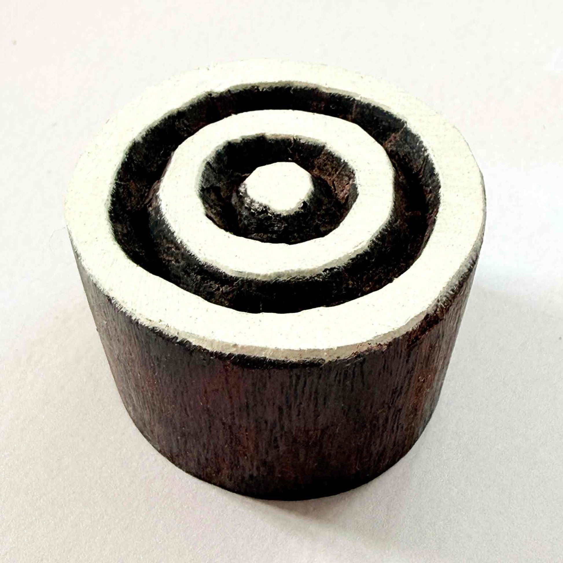 Indian wood block stamp — Target concentric circles resting on red-and-white patterned fabric, central dot and three even rings, hand-carved wooden stamp, classic traditional printing block ready for printing