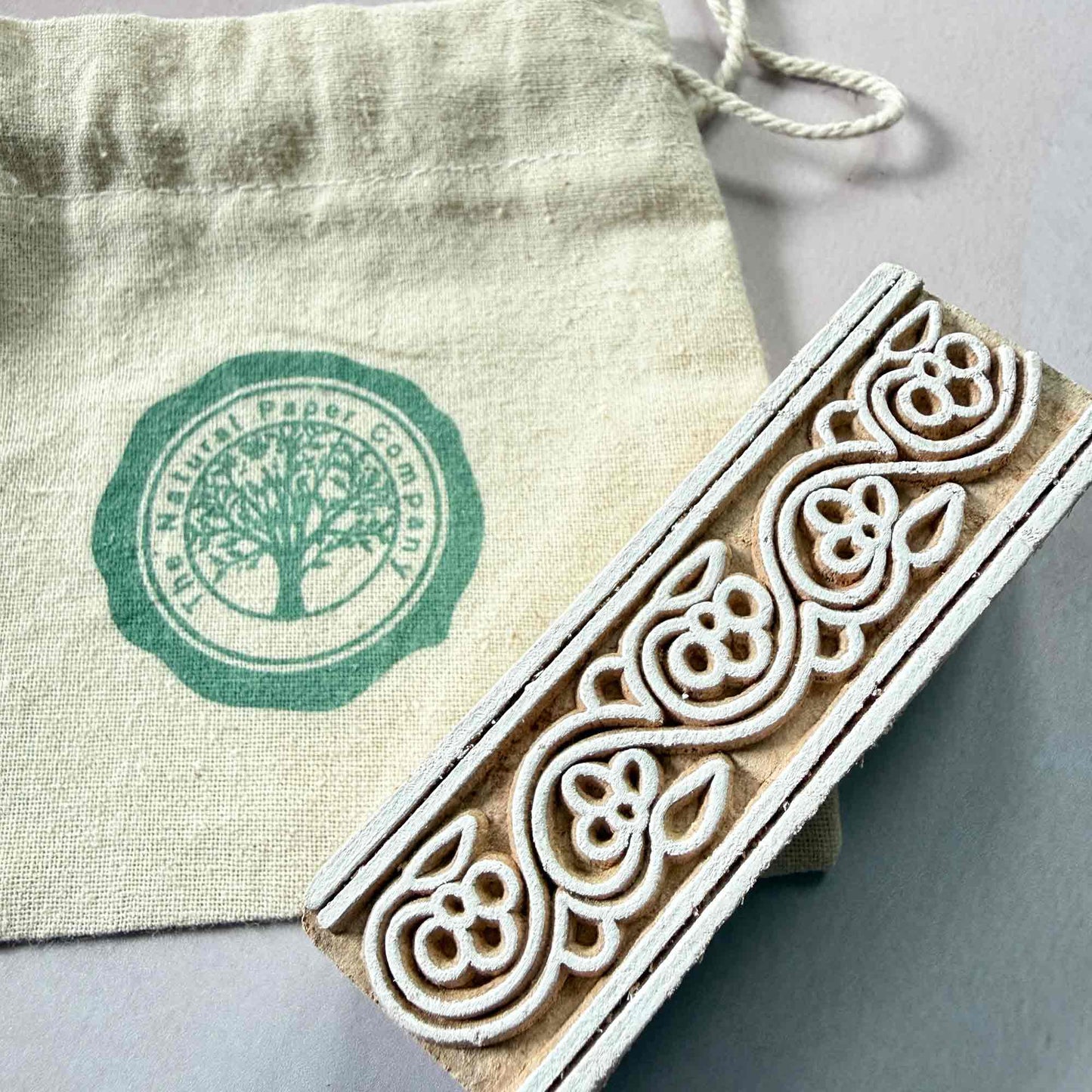 Decorative wooden stamp with intricate floral patterns on a branded gift bag from The Natural Paper Company.