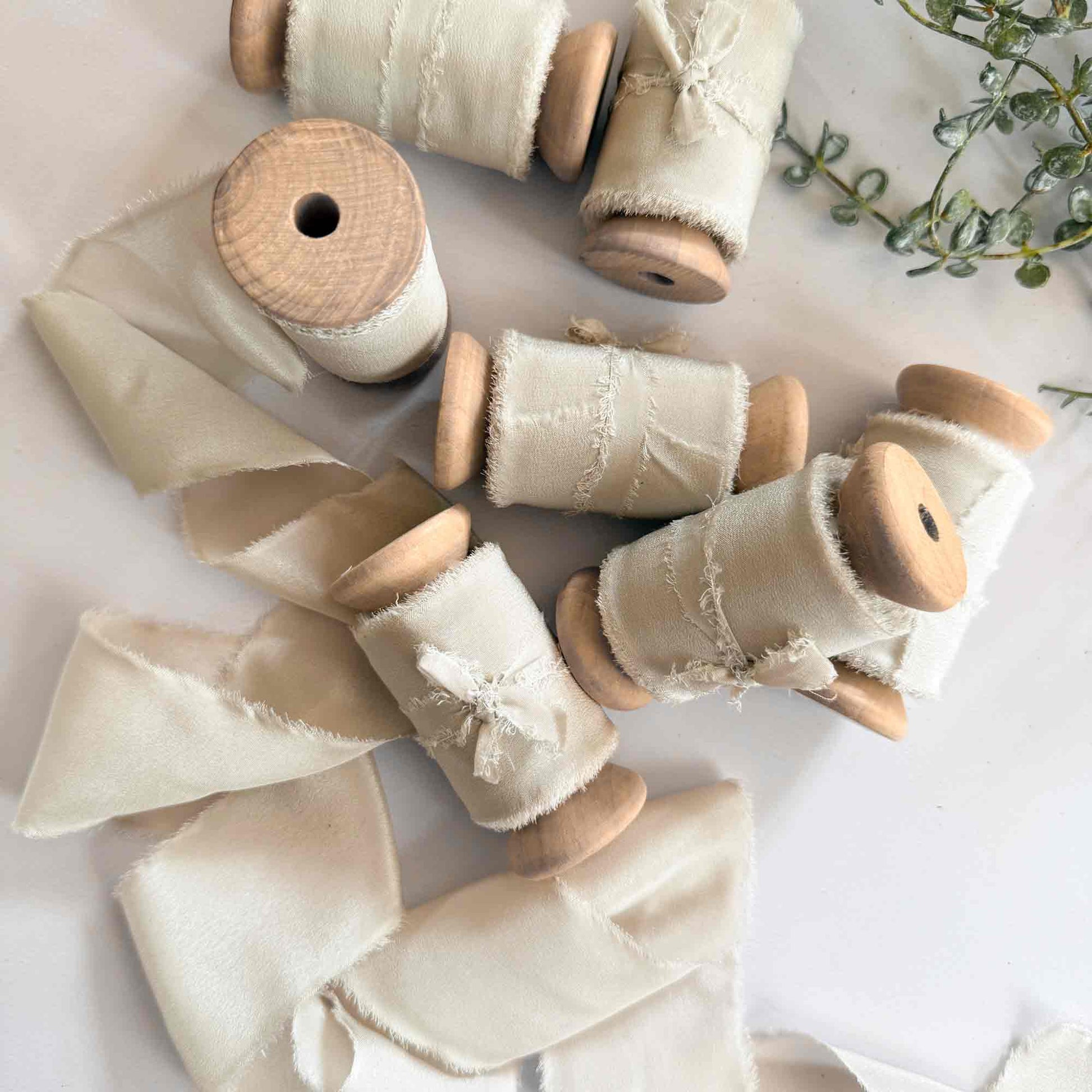 Wide silk ribbon on a wooden reel.  Neutral colour silk with a frayed edge