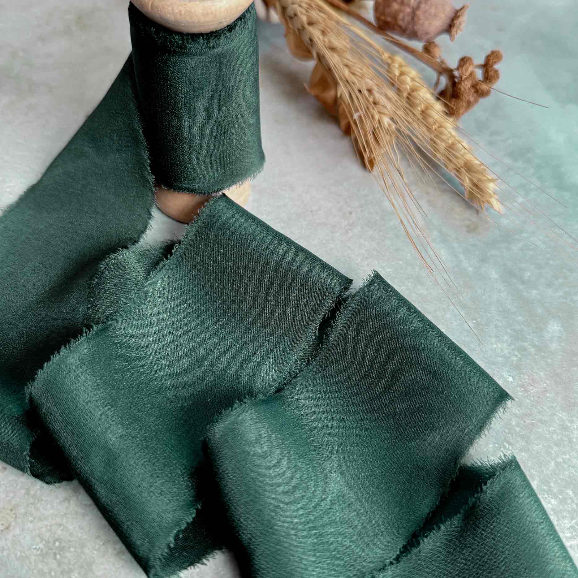 2 inch wide silk ribbon in dark green.  Frayed edge ribbon on a wooden reel.