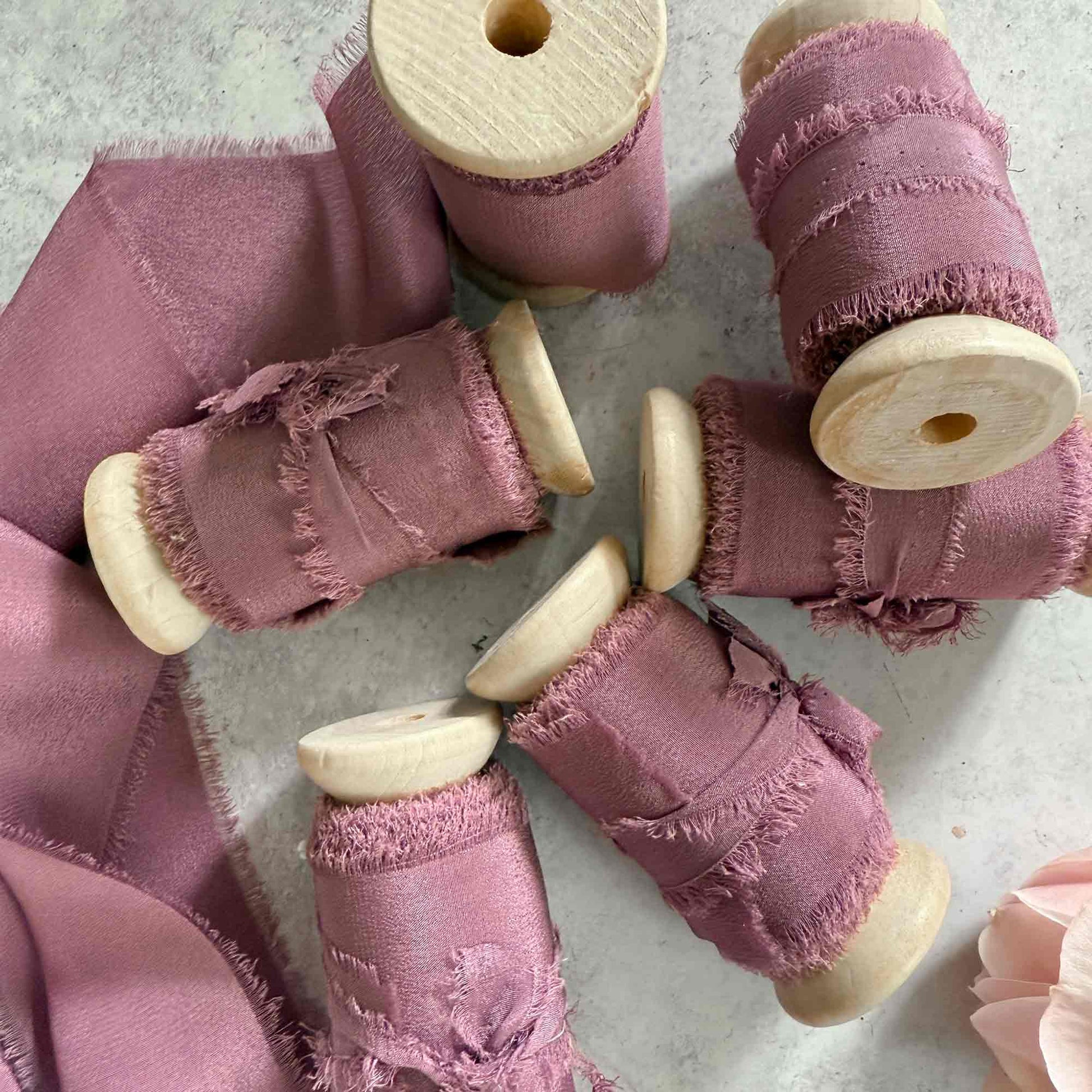wide silk ribbon on a wooden reel.  Mauve colour silk with a frayed edge