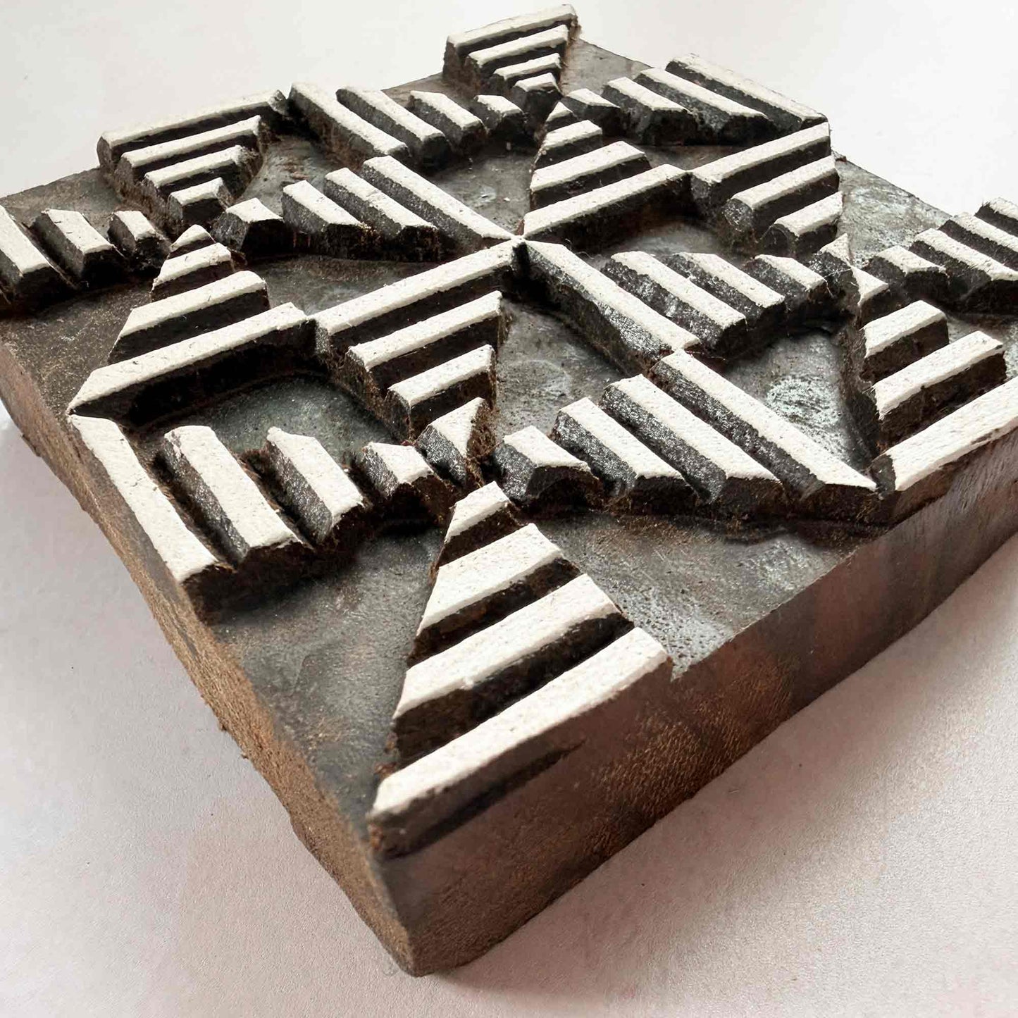 Hand-carved Windmill Indian wood block stamp — radiating geometric star motif viewed from a gentle angle, showing carved depth and fine lined texture, traditional hardwood printing block