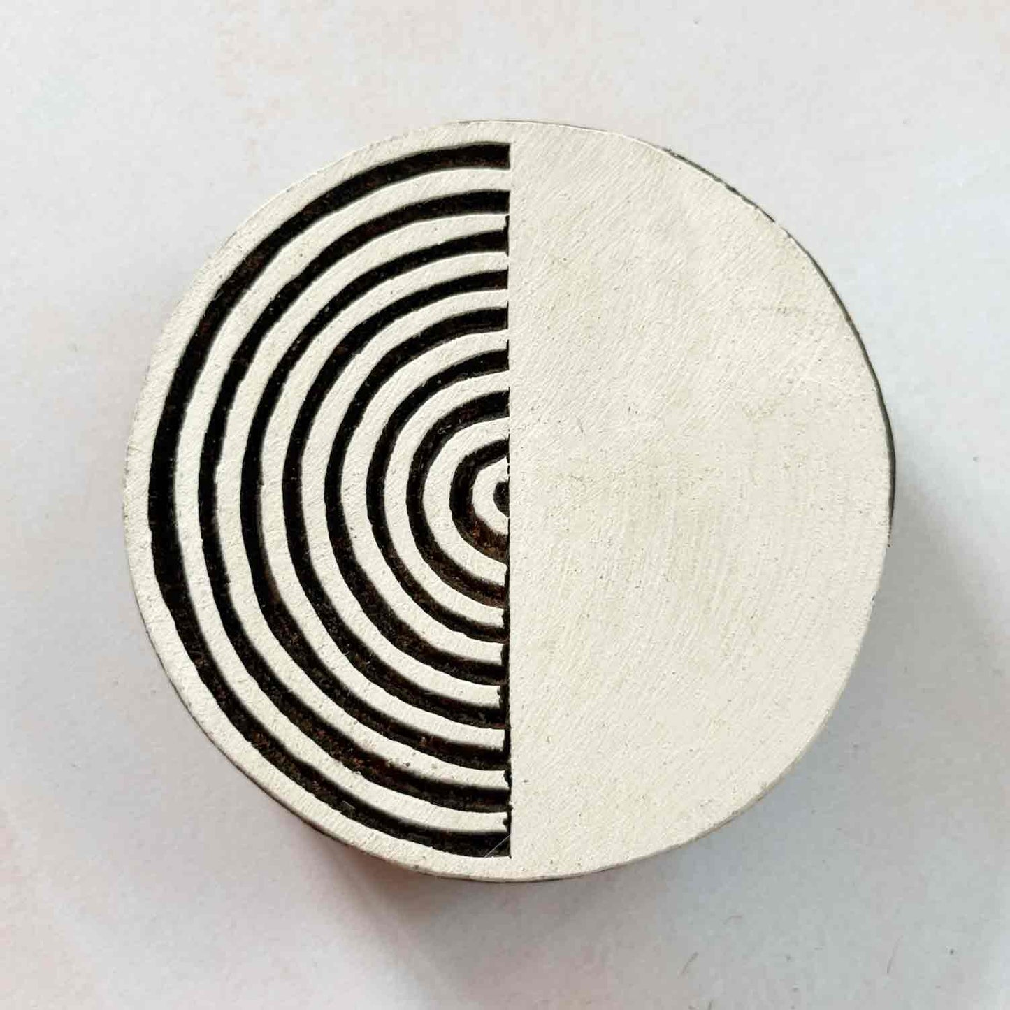 Indian wood block stamp — Yin split circle face-on view on pale background, half radiating arcs half solid, handcrafted wooden stamp, classic traditional printing block