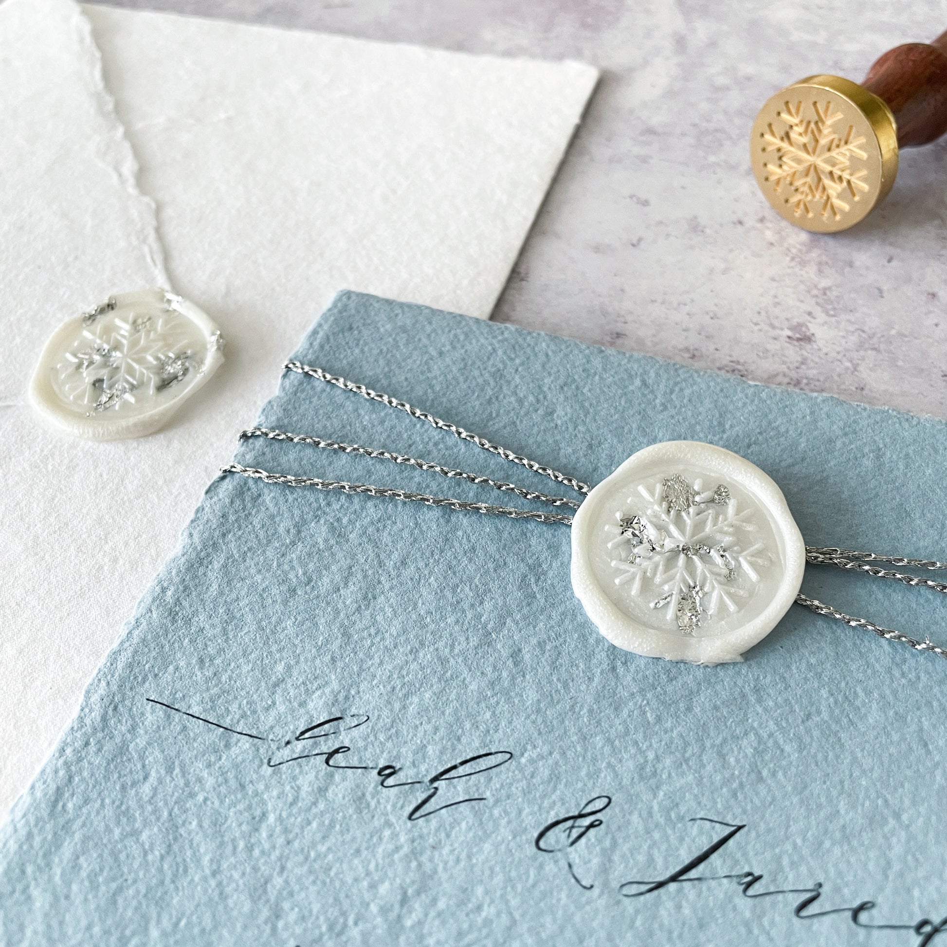 Snowflake wax seal.  Invitation made with pale blue hand made paper and pearlised white wax seal with snowflake print.  Silver, blue and white invitation