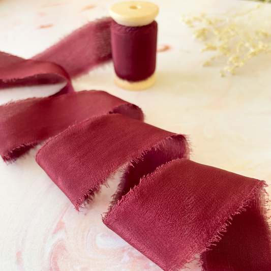 Burgundy habotai silk ribbon with a frayed edge.  Fine silk ribbon on a wooden reel.  Wine red silk
