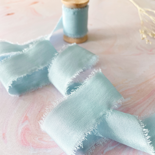 pale blue silk ribbon with a raw edge.  Habotai silk ribbon on a wooden reel.  1 inch wide silk ribbon
