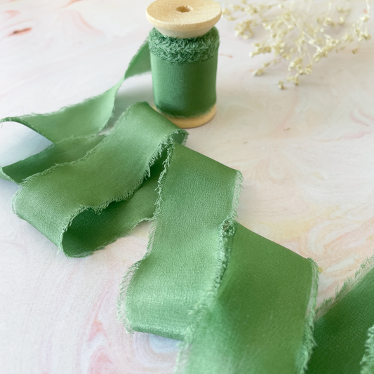 emerald green colour habotai silk ribbon on a wooden reel.  Delicate silk ribbon with a frayed edge.  Perfect for decorating wedding stationery