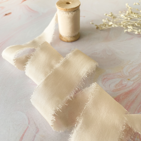 habotai silk ribbon in natural colour with torn edge.  Beige silk ribbon on wooden spool