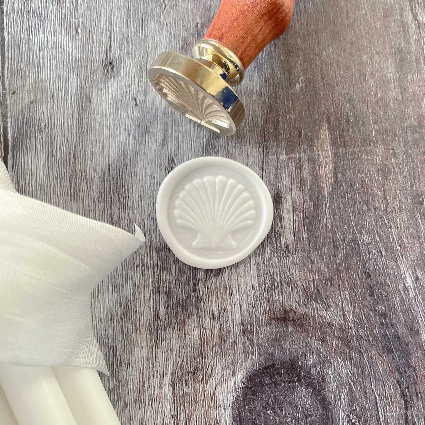 White wax seal with a seashell design.  Make coastal theme wax seals with our eco friendly sealing wax stamp.  Brass wax stamp with a wooden handle.  Perfect for decorating wedding invitations, stationery, envelopes, gift wrap and more.  By The Natural Paper Company