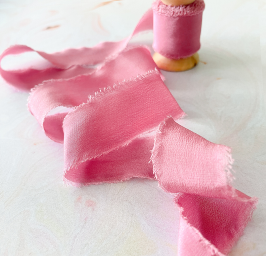 Raspberry pink silk ribbon with frayed edge.  Habotai silk ribbon on a wooden reel.  Luxury silk ribbon in pink