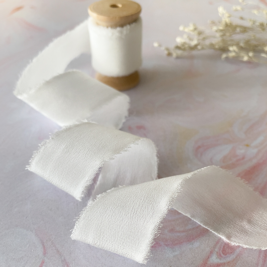 white habotai silk ribbon with frayed edge.  Luxury silk ribbon on wooden spool